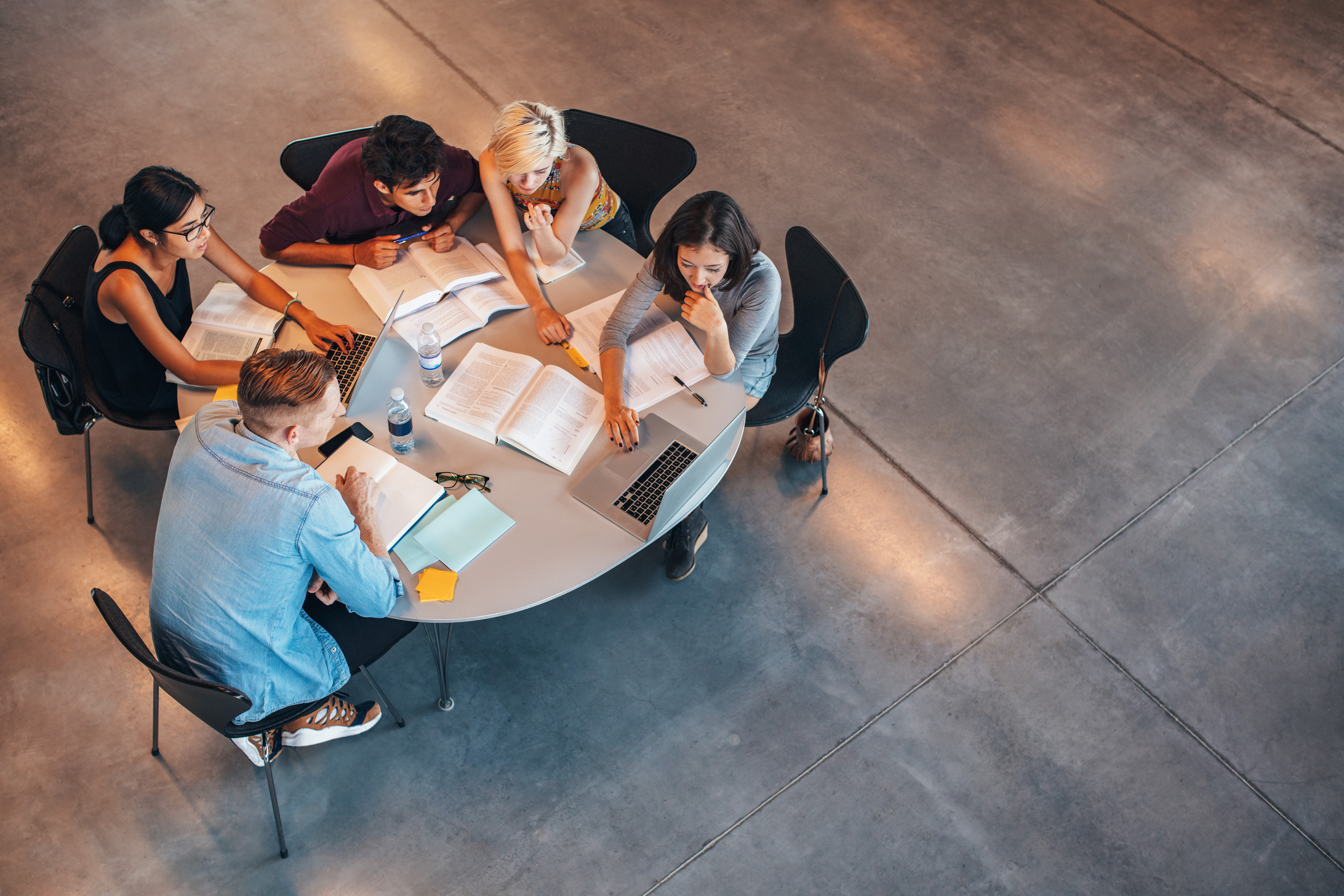 Multiracial group of young students studying together. High angle shot of young people sitting at the table and studying on laptop computer.