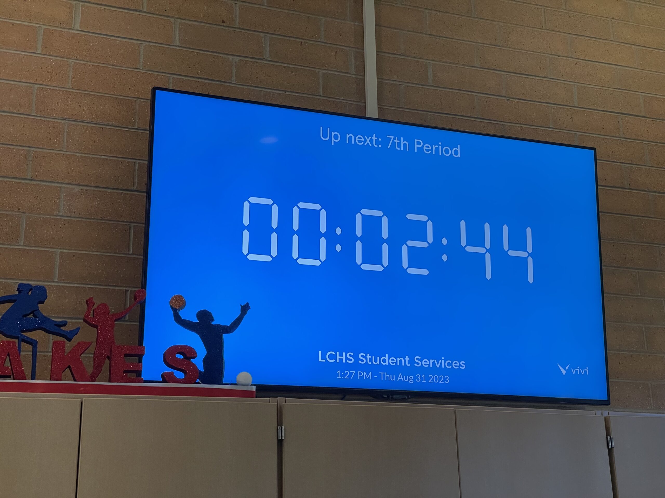 A flat panel display shows a countdown timer on the wall of a school hallway, helping students know how much more time they have before the bell rings.