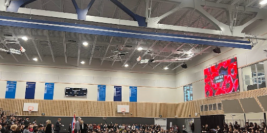 Upper school gymnasium full of students sitting on the bleachers for a school assembly.
