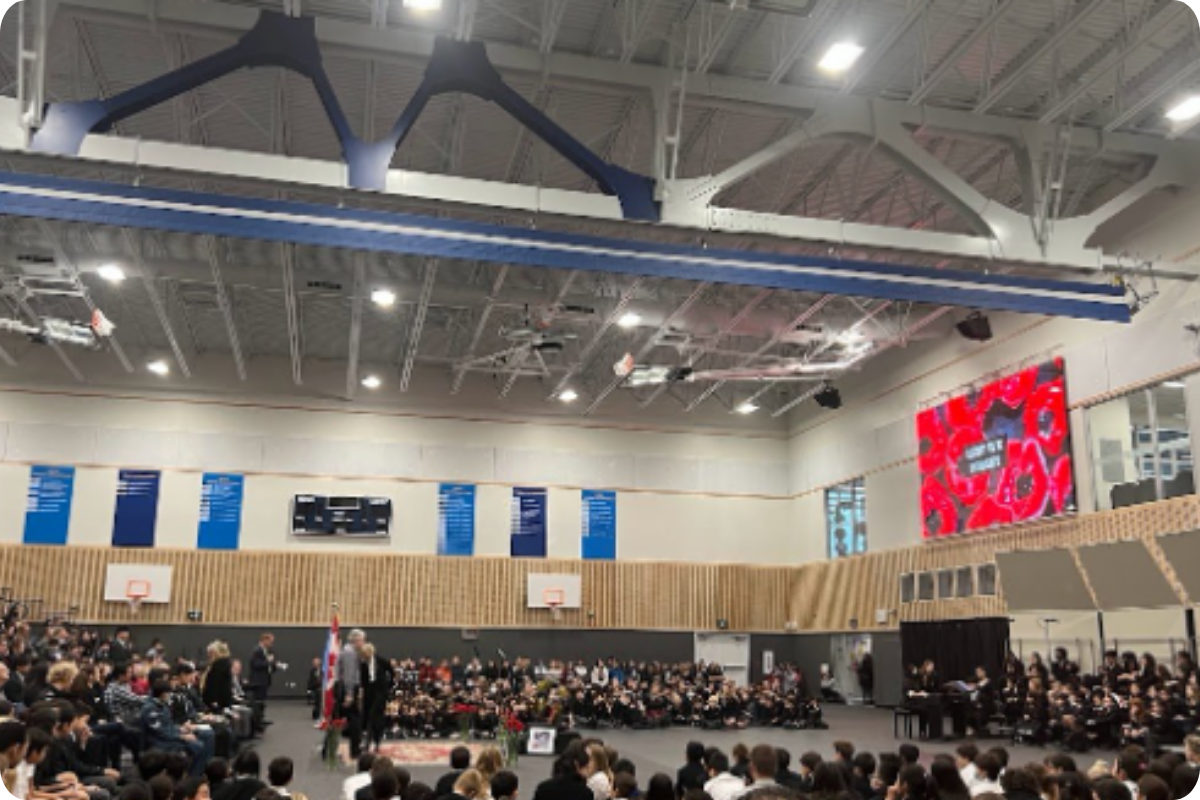 Upper school gymnasium full of students sitting on the bleachers for a school assembly.