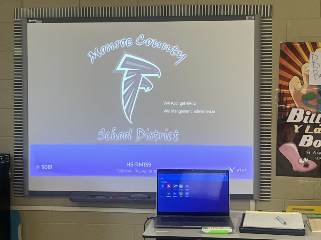 A classroom with an interactive whiteboard displaying the school district's logo and digital tool information.