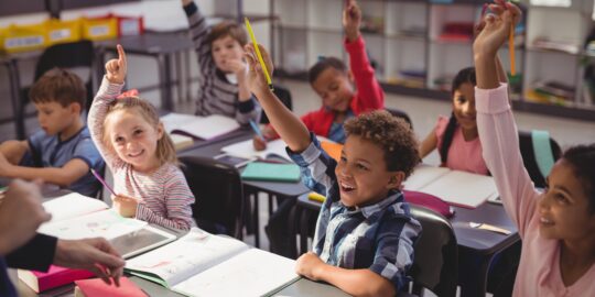 Schoolkids raising their hands in classroom