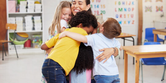 Teacher is hugged by students in a classroom
