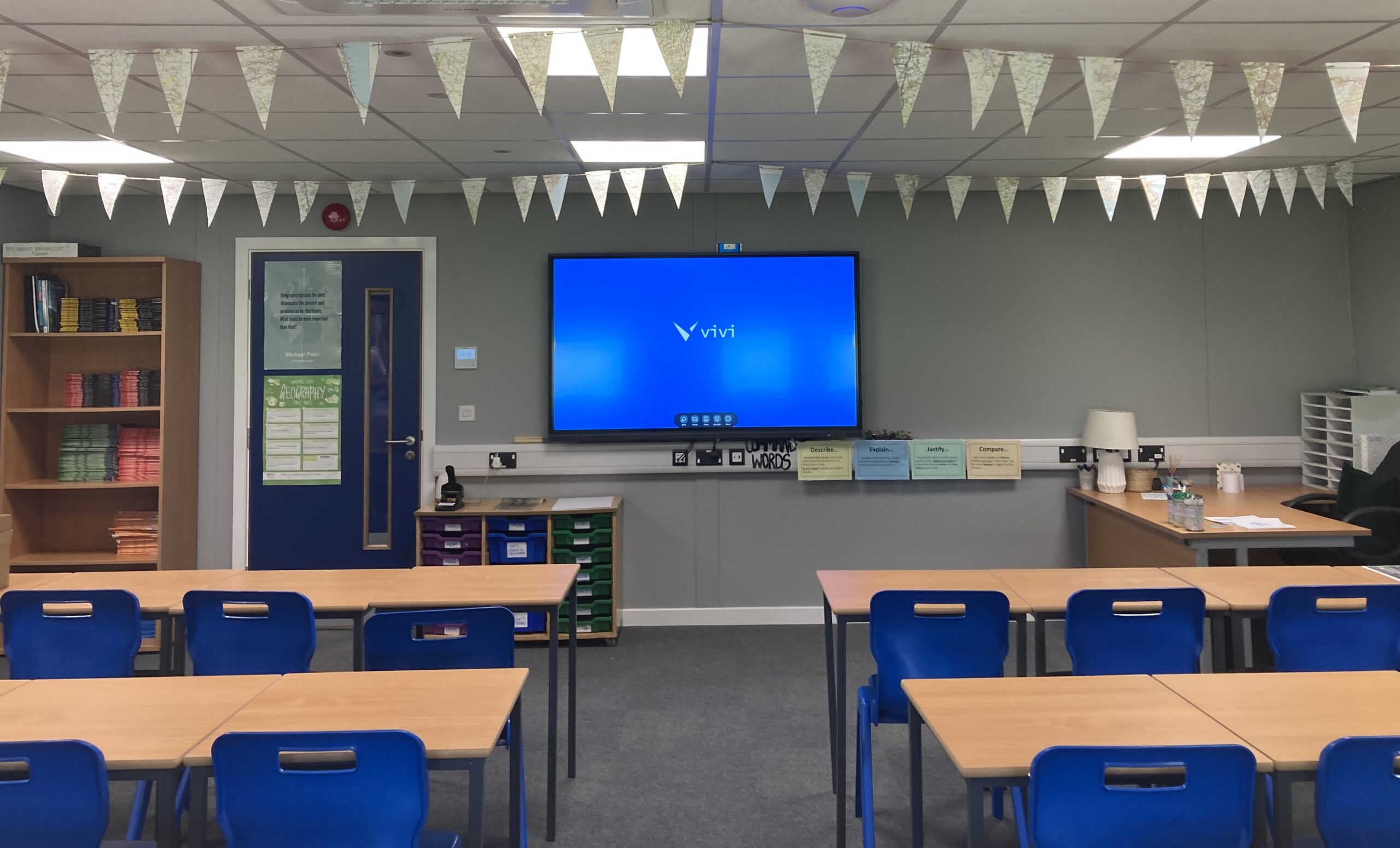 A school classroom with Vivi seen on TV display.