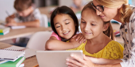 Teacher helping pupils with digital tablet