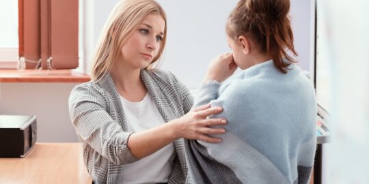 Young teacher sits at a desk in class and talks to a new student