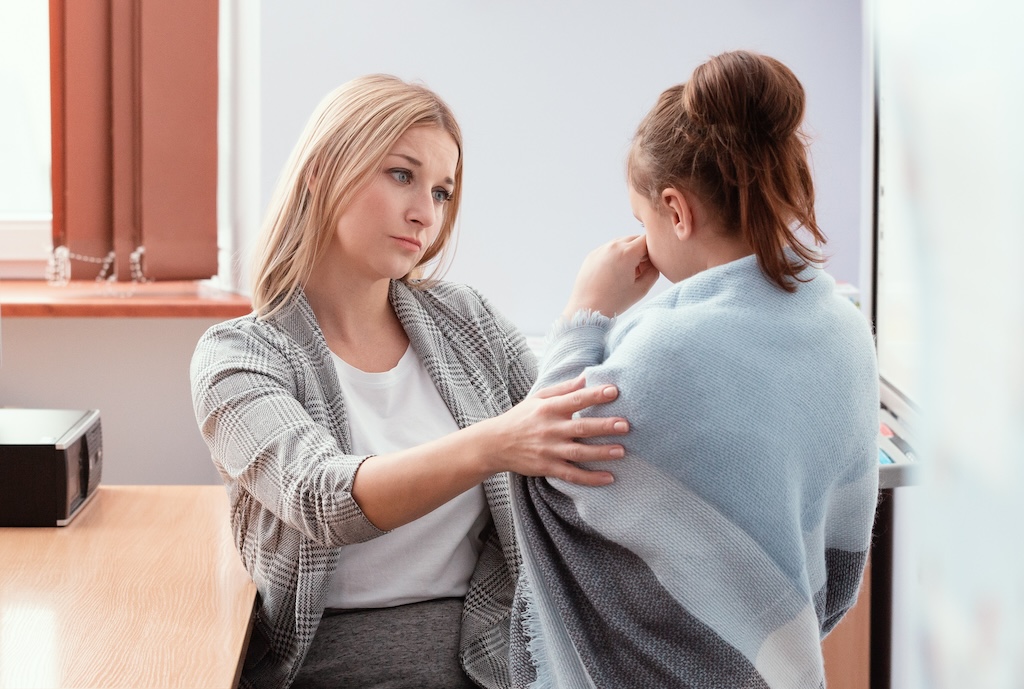 top 10 trauma-informed teaching strategies for educators 1 Young teacher sits at a desk in class and talks to a new student