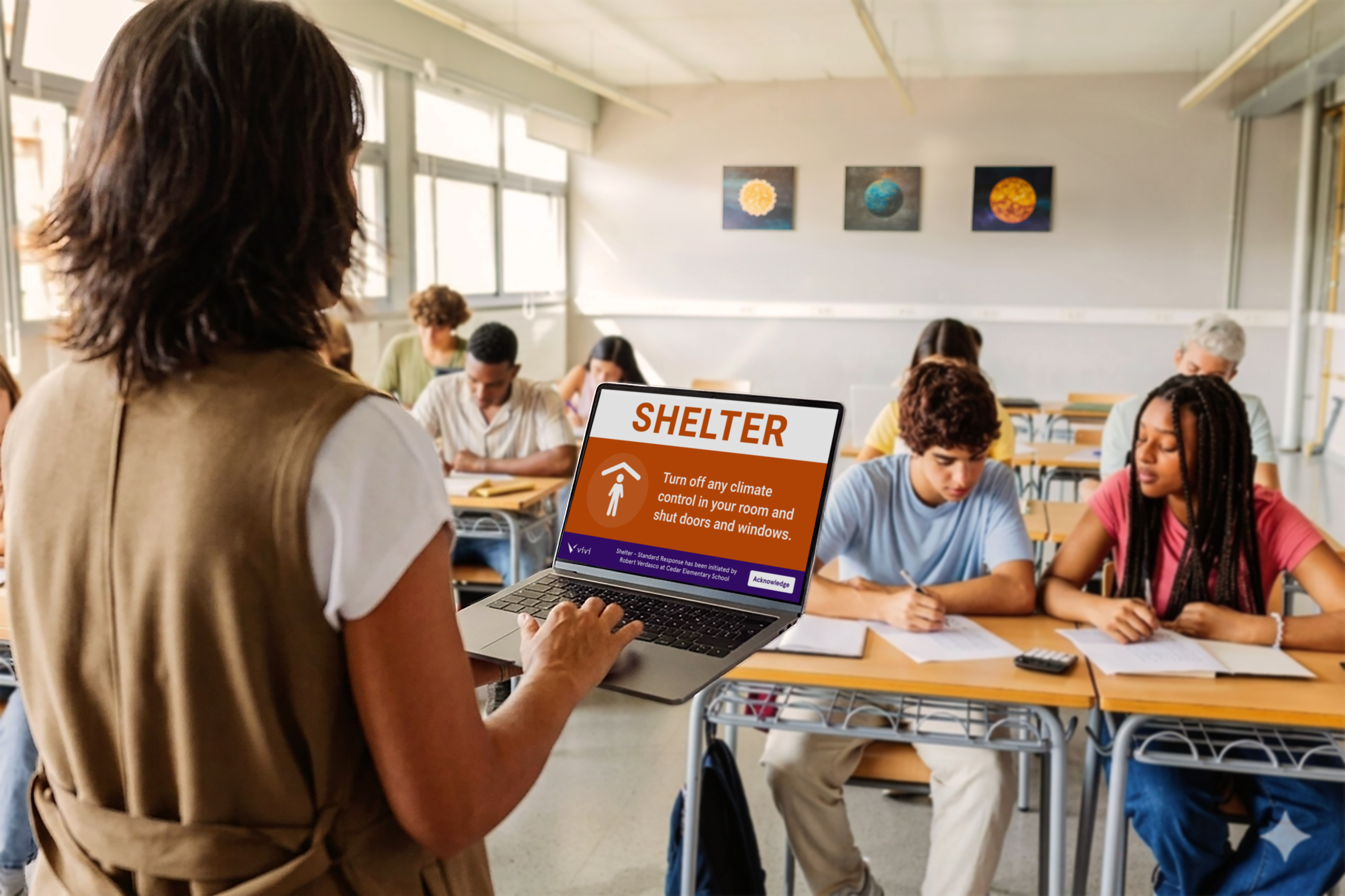 A wide shot of a bright, contemporary classroom. Students are focused on a group task or lab activity. A teacher sees an emergency alert on their device