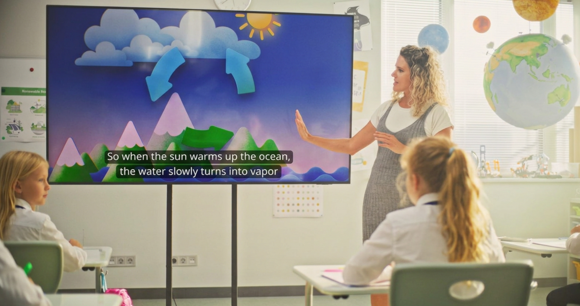 A teacher at the front of a UK classroom. Live captions appear on the interactive display and on individual pupil devices.